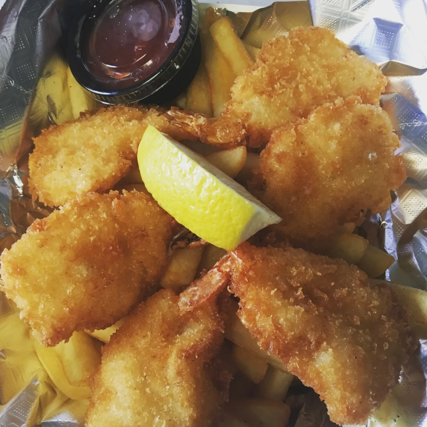Basket of breaded shrimp over fries with cocktail sauce and a lemon wedge.