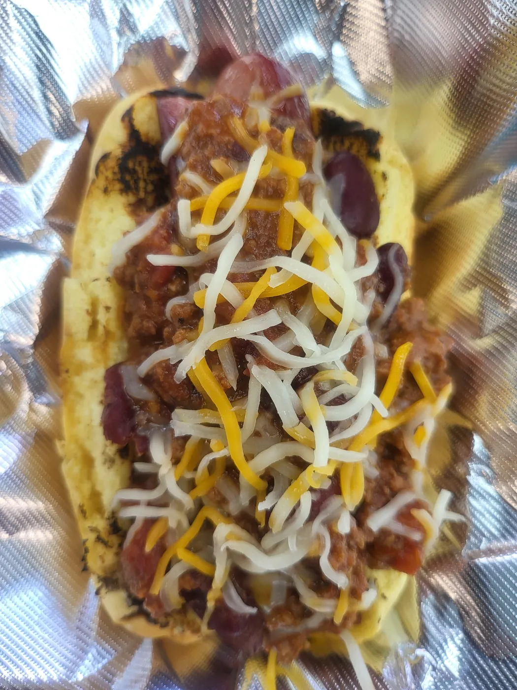 Chili cheese dog topped with shredded cheese on a toasted bun.