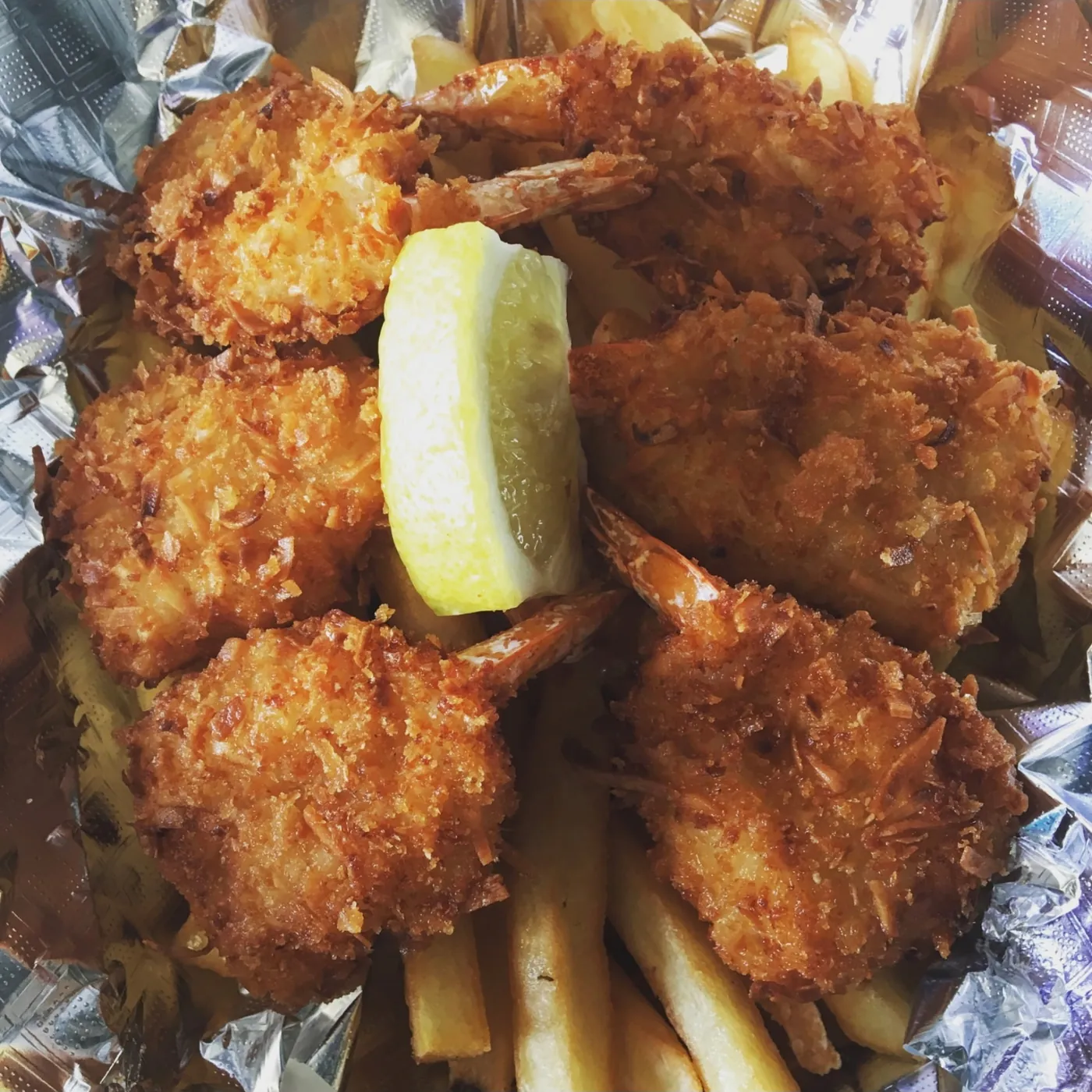 Golden coconut shrimp over fries with a lemon slice.