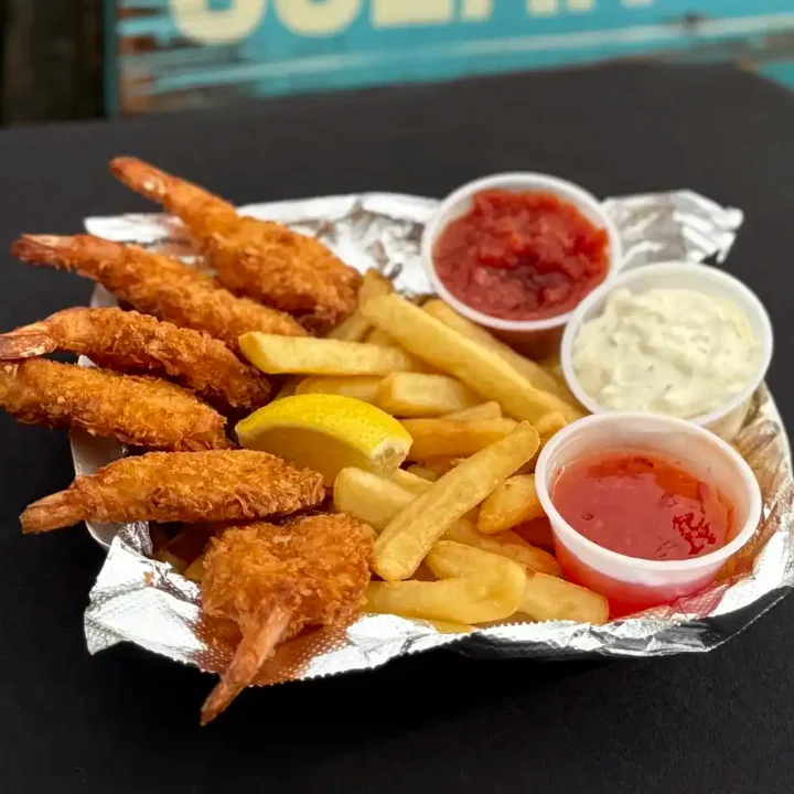 Fried shrimp served with fries and dipping sauces in a foil boat.