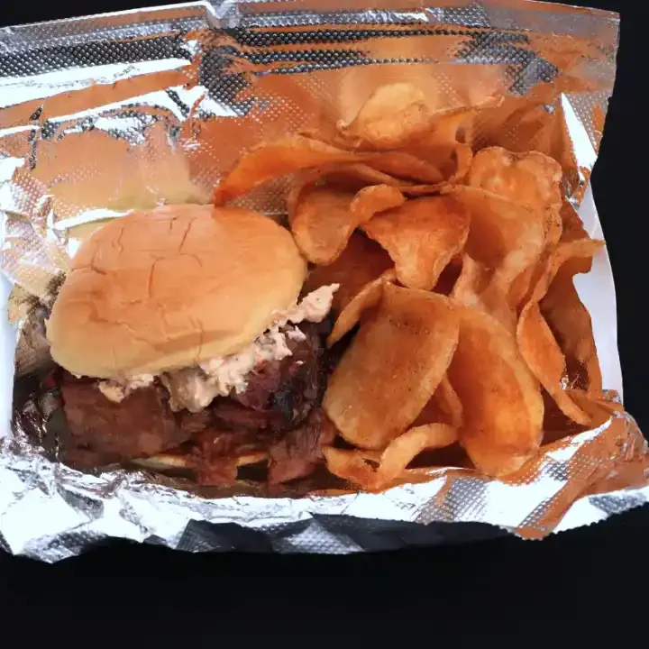 BBQ beef brisket sandwich topped with crab dip on a potato bun, served with homemade chips.