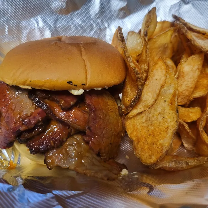 BBQ beef brisket sandwich on a toasted potato bun with homemade chips.