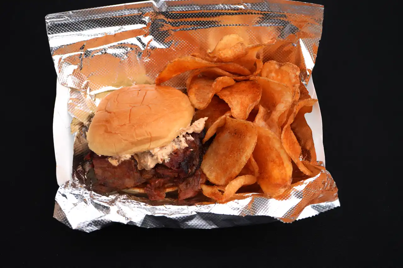 BBQ beef brisket sandwich topped with crabdip, served with chips